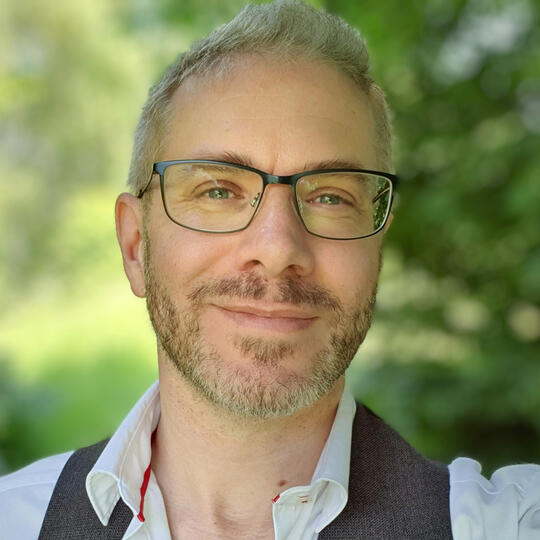 Portrait of Finbarre Snarey wearing glasses and a white shirt with a waistcoat, photographed outdoors.