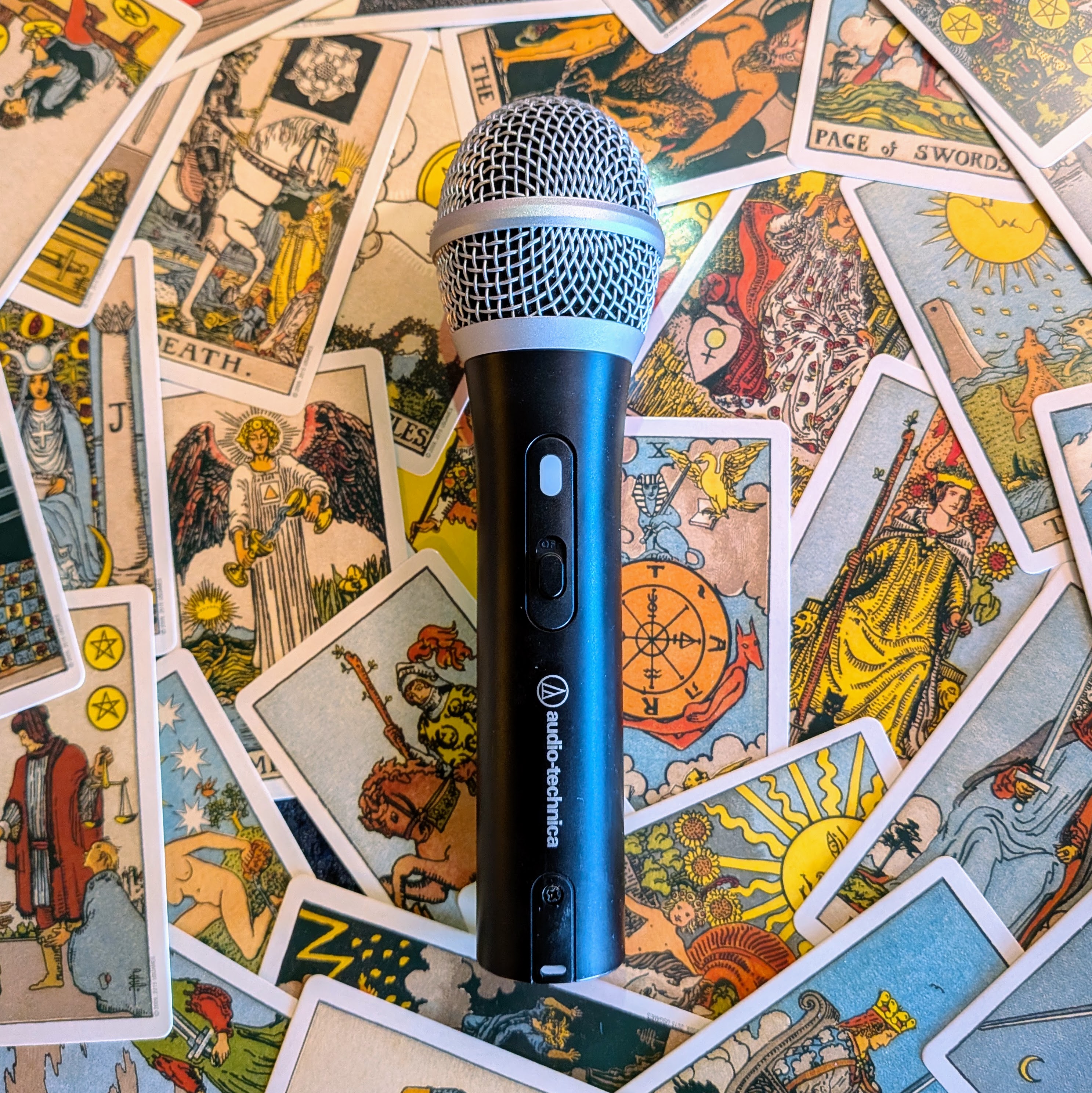 Black handheld microphone resting on a spread of Rider-Waite-Smith tarot cards.